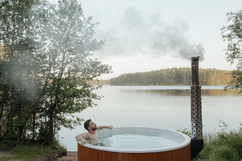 pexels-photo-8844584 Man enjoying a serene soak in an outdoor hot tub by a peaceful lake surrounded by nature.